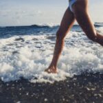 Barefoot Running - Side view of crop anonymous fit young female in white swimwear running on beach along waving sea during summer vacation