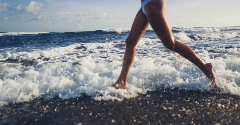 Barefoot Running - Side view of crop anonymous fit young female in white swimwear running on beach along waving sea during summer vacation