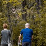 Trail Recovery - Back view of unrecognizable male in orthosis on broken leg walking with woman on path in park