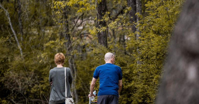 Trail Recovery - Back view of unrecognizable male in orthosis on broken leg walking with woman on path in park