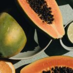 Triathlete's Diet - Top view of halves of ripe papaya together with oranges and limes placed on green round dishes and green fabric on white background