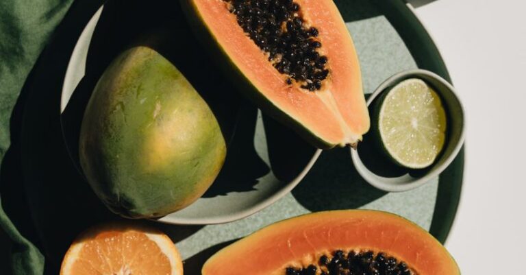 Triathlete's Diet - Top view of halves of ripe papaya together with oranges and limes placed on green round dishes and green fabric on white background