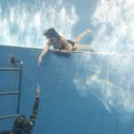 Swim Pull - Anonymous couple swimming underwater in pool near hole