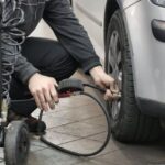 Tire Maintenance - Man in Black Jacket and Black Pants Sitting Near Silver Vehicle