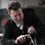 Bike Maintenance - Concentrated male biker in casual wear fixing motorcycle part while working in garage