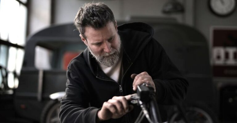 Bike Maintenance - Concentrated male biker in casual wear fixing motorcycle part while working in garage