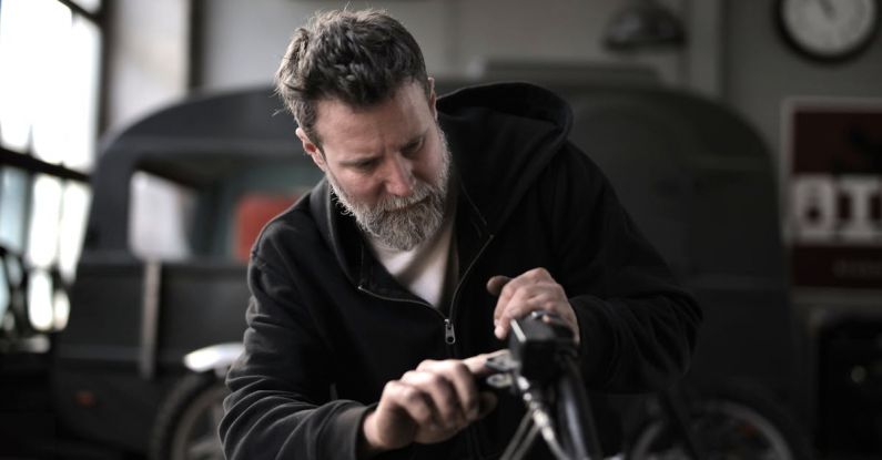 Bike Maintenance - Concentrated male biker in casual wear fixing motorcycle part while working in garage