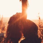 Dynamic Stretching - Side view of graceful woman leaning back with raised leg while dancing between shrubs in countryside in back lit