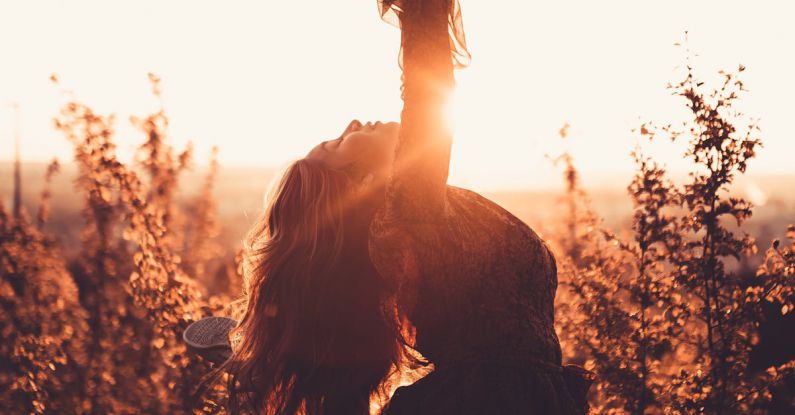 Dynamic Stretching - Side view of graceful woman leaning back with raised leg while dancing between shrubs in countryside in back lit